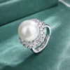 Single adjustable open ring with double halo cubic zirconia surrounding round white pearl close-up shot on green fabric background