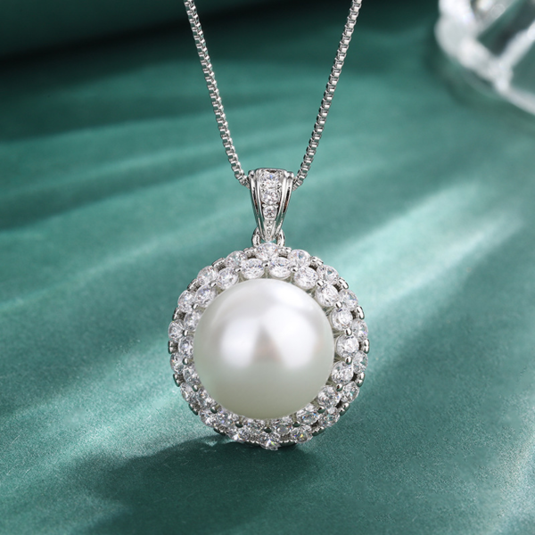 Macro close-up shot double halo cubic zirconia surrounded round pearl pendant necklace on textured green fabric
