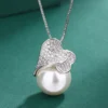 Double heart pave cubic zirconia imitation pearl necklace pendant with silver box chain, shot on solid green background, focus on heart setting and large pearl texture