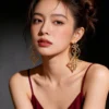 Female model bilateral wearing pair hollow four leaf clover long drop gold earrings full upper body shot
