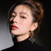 Female model single ear closeup wearing hollow four leaf clover geometric long gold drop earrings