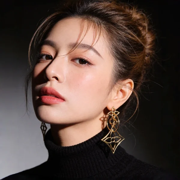 Female model single ear closeup wearing hollow four leaf clover geometric long gold drop earrings