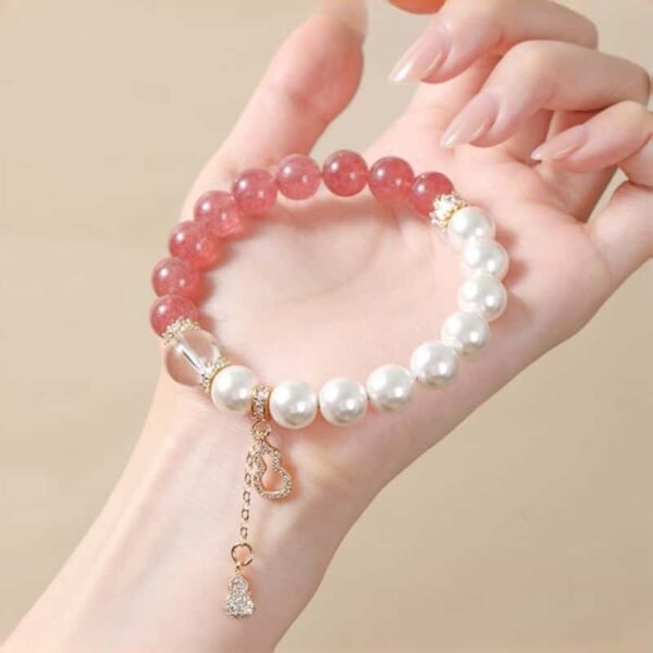 Delicate strawberry quartz and imitation pearl bracelet with gourd pendant held in a hand