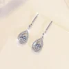 Top-down overhead flat lay photo pair S925 sterling silver 0.5ct moissanite teardrop dangle earrings, fully unfolded symmetrical layout, full hook and pendant detail visible
