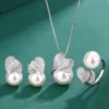 Overhead flat lay complete layout photo of double heart CZ imitation pearl 3pcs jewelry set: earrings, necklace pendant, open ring arranged on green background
