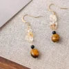 Close-up texture photo handmade tiger eye citrine chip black agate dangle earrings laid on woven linen fabric, highlighting natural stone luster and bead detail