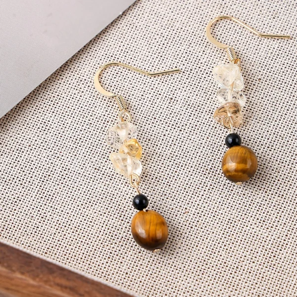 Close-up texture photo handmade tiger eye citrine chip black agate dangle earrings laid on woven linen fabric, highlighting natural stone luster and bead detail