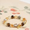 Natural yellow rutilated quartz bracelet with tiger eye citrine and Chinese gourd coin charm on floral background